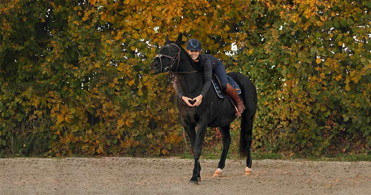 Reiterin auf Pferd vor Bäumen. Sie form ein Herz mit ihren Händen.