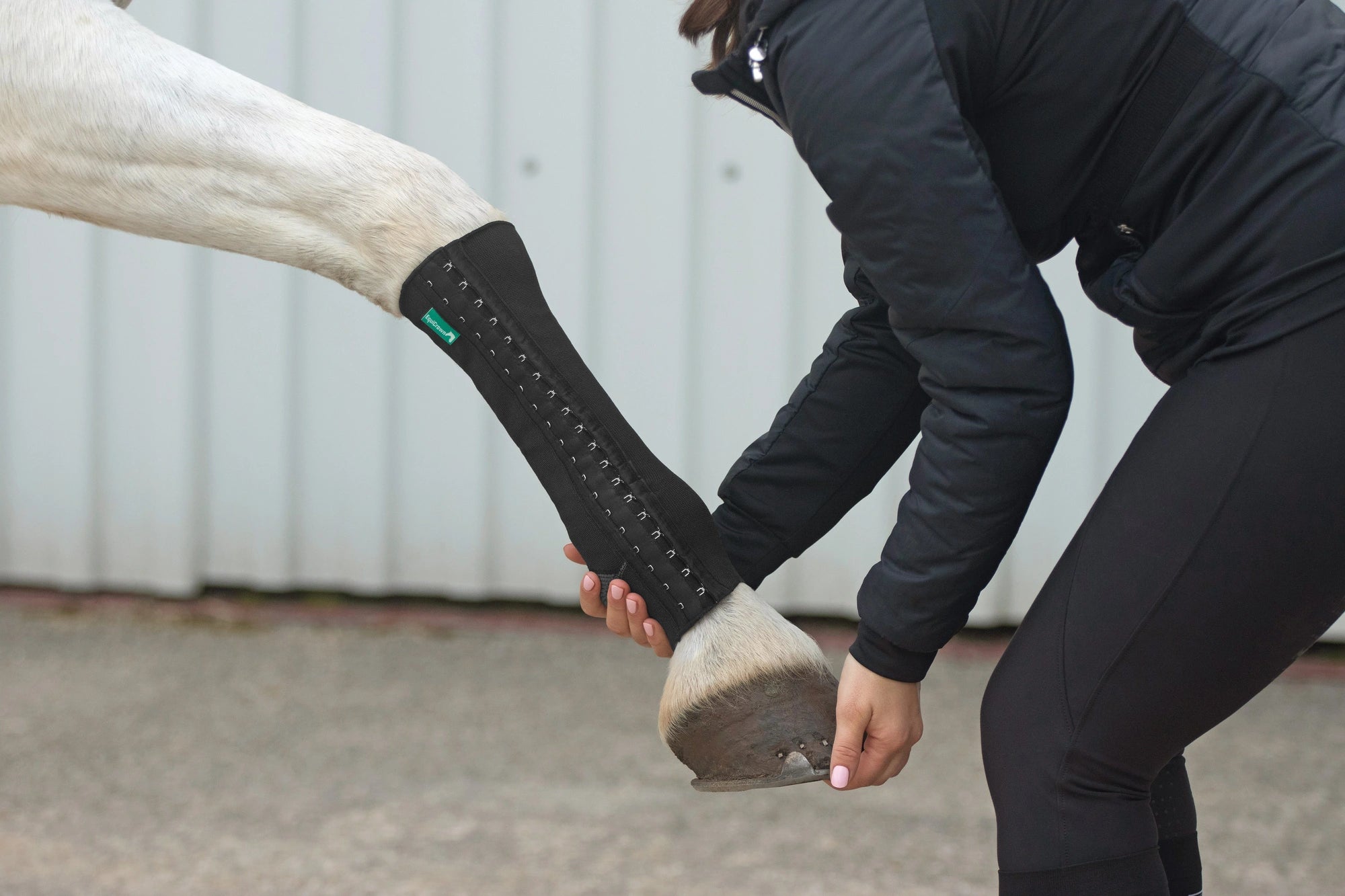 Frau hält Huf ihres Pferdes. Das Pferd trägt die EquiCrown fit Bandage an seinem Bein.